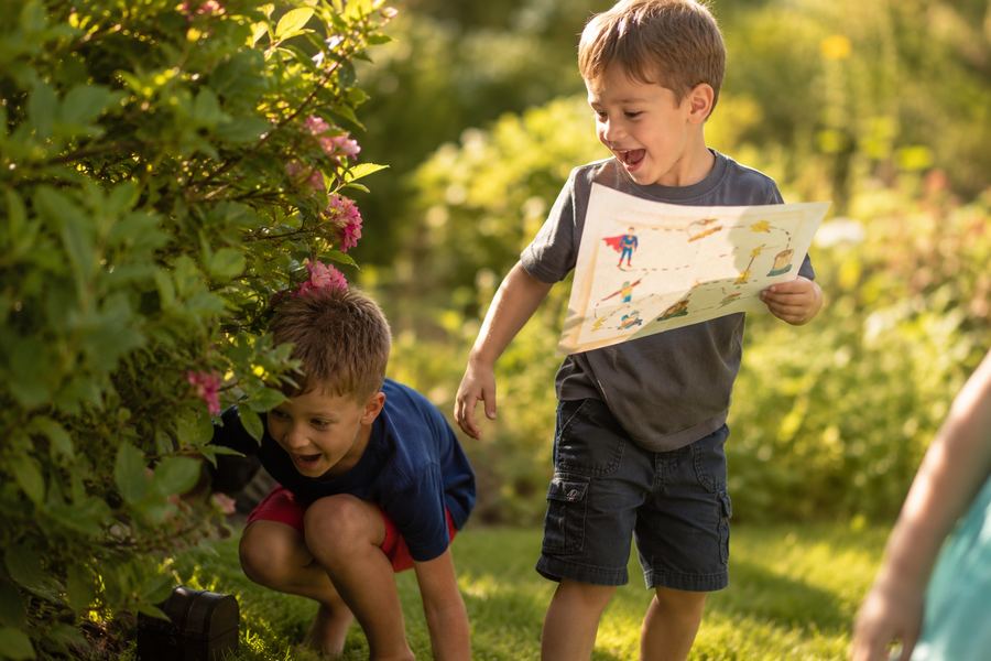 Deux enfants suivent la carte au trésor KidoTrésor dans le jardin